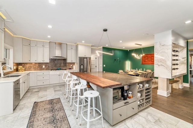 kitchen featuring sink, stainless steel appliances, wall chimney exhaust hood, white cabinets, and hanging light fixtures