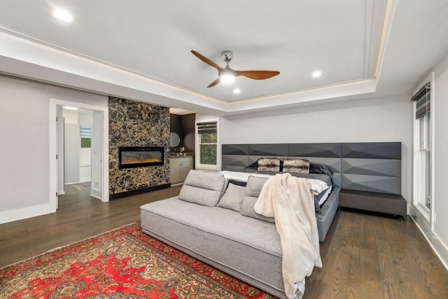 bedroom featuring a fireplace, dark wood-type flooring, ceiling fan, and a tray ceiling