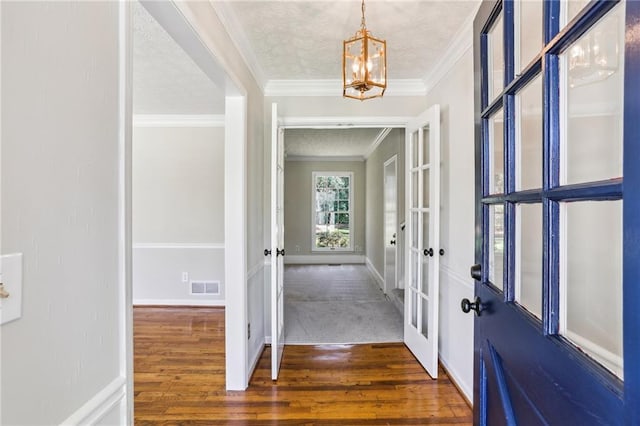 entrance foyer with a textured ceiling, wood finished floors, visible vents, baseboards, and ornamental molding