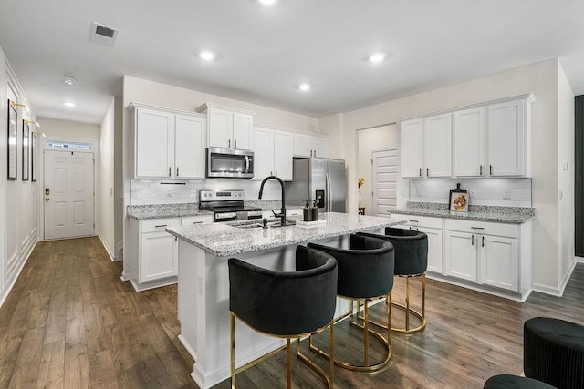 kitchen with appliances with stainless steel finishes, a center island with sink, and white cabinetry