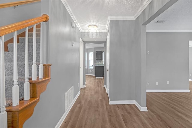 corridor featuring hardwood / wood-style flooring, crown molding, and a textured ceiling