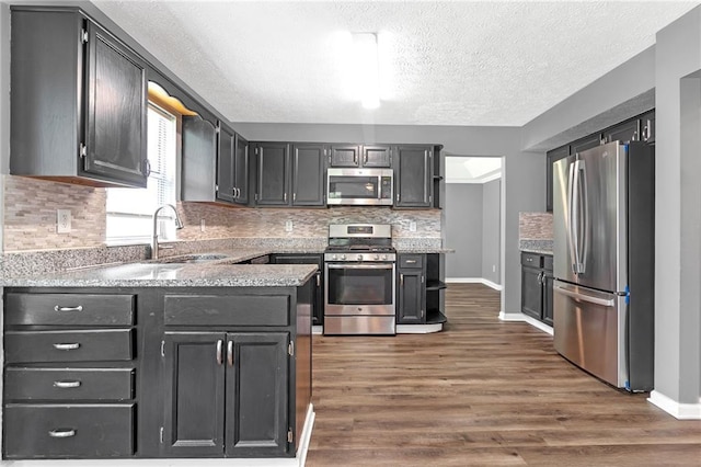 kitchen with sink, appliances with stainless steel finishes, tasteful backsplash, a textured ceiling, and dark hardwood / wood-style flooring