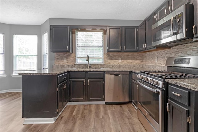 kitchen with tasteful backsplash, sink, dark stone countertops, light hardwood / wood-style floors, and stainless steel appliances