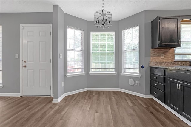 unfurnished dining area featuring a textured ceiling, a chandelier, and light wood-type flooring