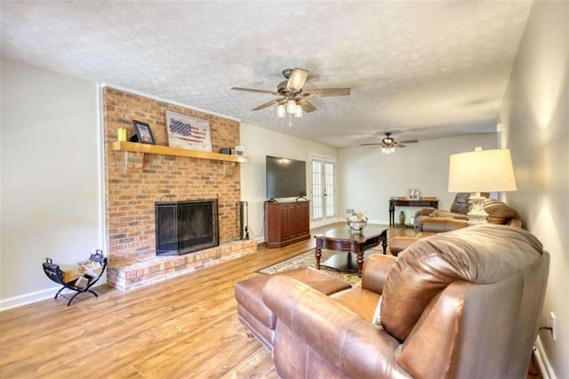 living room featuring ceiling fan, a textured ceiling, light hardwood / wood-style floors, and a brick fireplace