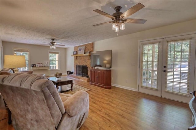 living room with french doors, a textured ceiling, a fireplace, ceiling fan, and light wood-type flooring