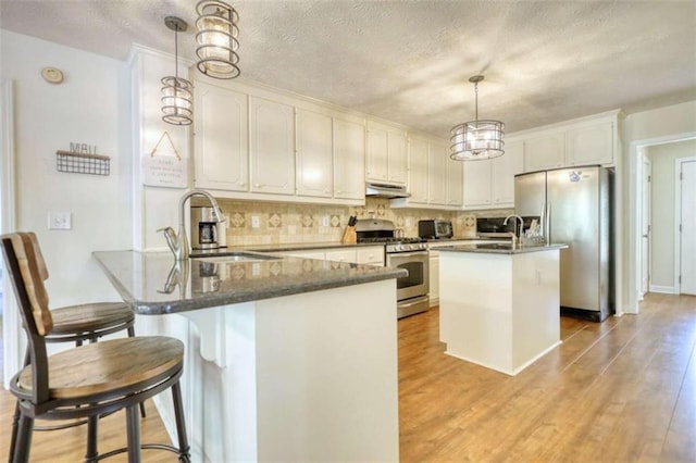 kitchen featuring stainless steel appliances, sink, an island with sink, white cabinetry, and decorative light fixtures