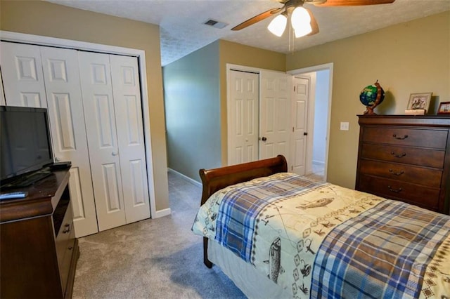 bedroom featuring a textured ceiling, multiple closets, light carpet, and ceiling fan