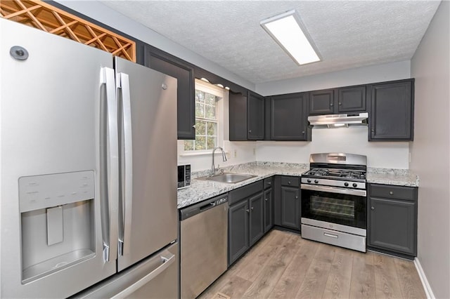 kitchen with appliances with stainless steel finishes, light hardwood / wood-style flooring, light stone counters, and sink