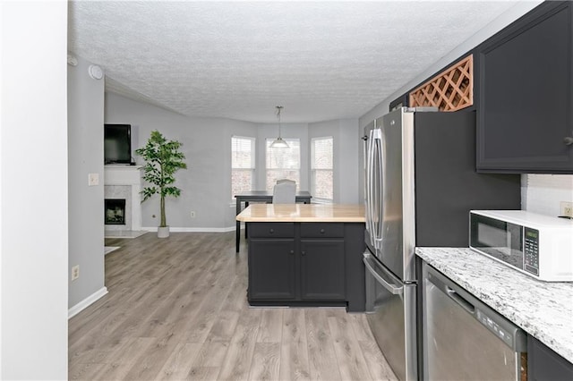 kitchen featuring a textured ceiling, dishwasher, decorative light fixtures, light wood-type flooring, and a high end fireplace