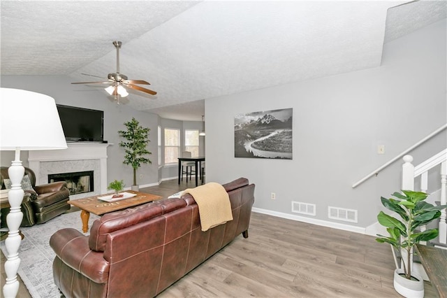 living room with a high end fireplace, light wood-type flooring, ceiling fan, a textured ceiling, and lofted ceiling