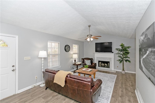 living room with ceiling fan, light wood-type flooring, lofted ceiling, and a textured ceiling