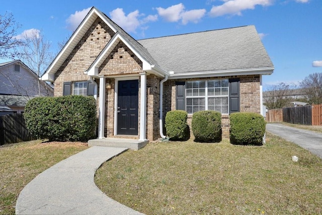 view of front facade featuring roof with shingles, a front yard, fence, and brick siding