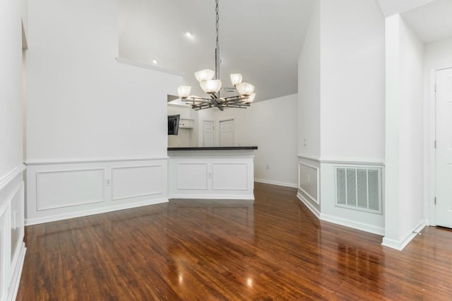 unfurnished dining area with visible vents, wood finished floors, a chandelier, and a decorative wall