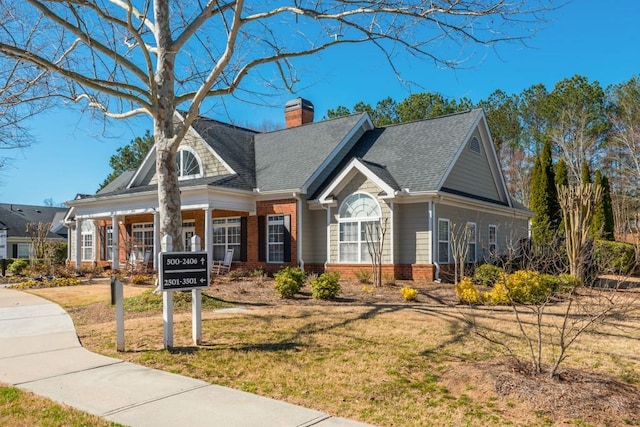 view of front facade featuring brick siding, a chimney, a front yard, and a shingled roof