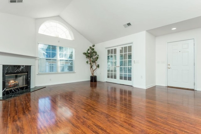 unfurnished living room featuring baseboards, a fireplace, french doors, wood finished floors, and high vaulted ceiling