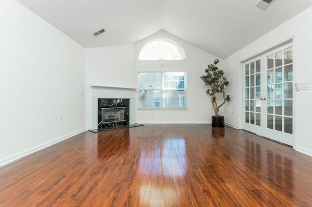 unfurnished living room with a high end fireplace, visible vents, vaulted ceiling, and wood finished floors