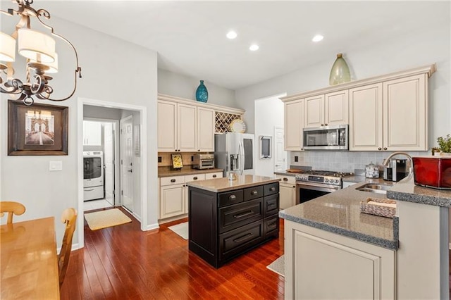kitchen with appliances with stainless steel finishes, a sink, washer / clothes dryer, tasteful backsplash, and dark wood-style flooring