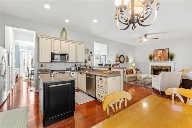 kitchen with appliances with stainless steel finishes, dark wood-style flooring, backsplash, a kitchen island, and a chandelier