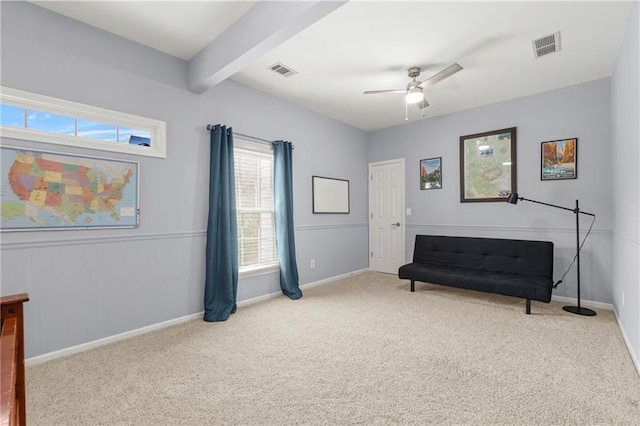sitting room with a ceiling fan, carpet floors, baseboards, and beamed ceiling