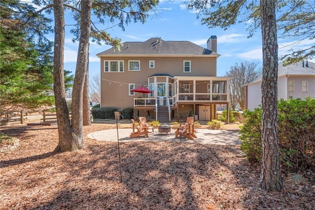 rear view of property featuring an outdoor fire pit, a sunroom, a chimney, a patio area, and a wooden deck