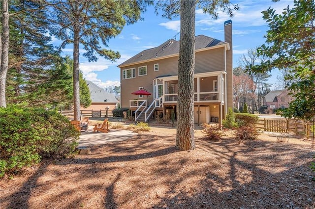 back of property with a sunroom, a chimney, a patio area, stairs, and fence