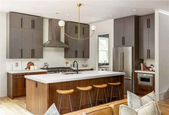 kitchen featuring a kitchen bar, wall chimney range hood, sink, and appliances with stainless steel finishes