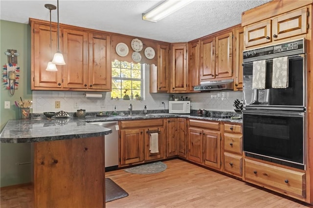 kitchen with a peninsula, brown cabinetry, dobule oven black, white microwave, and dishwasher