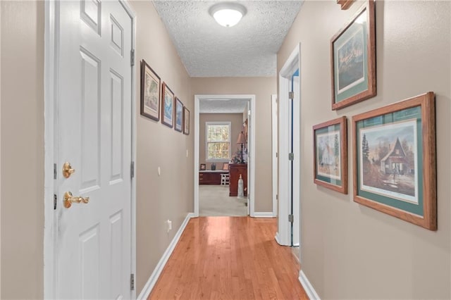 corridor featuring a textured ceiling, baseboards, and light wood-type flooring