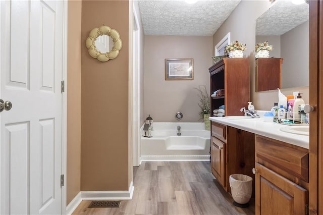 bathroom with wood finished floors, a textured ceiling, visible vents, double vanity, and a garden tub
