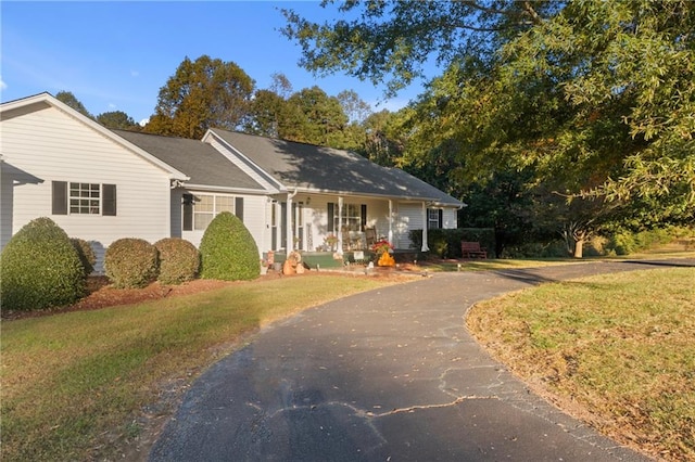 ranch-style house featuring covered porch, driveway, and a front lawn