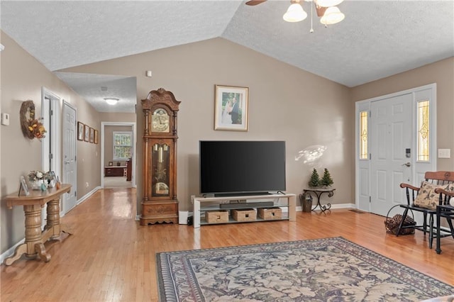 living area with a textured ceiling, baseboards, wood finished floors, and lofted ceiling