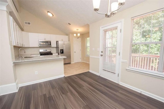 kitchen with appliances with stainless steel finishes, white cabinetry, kitchen peninsula, dark hardwood / wood-style flooring, and pendant lighting