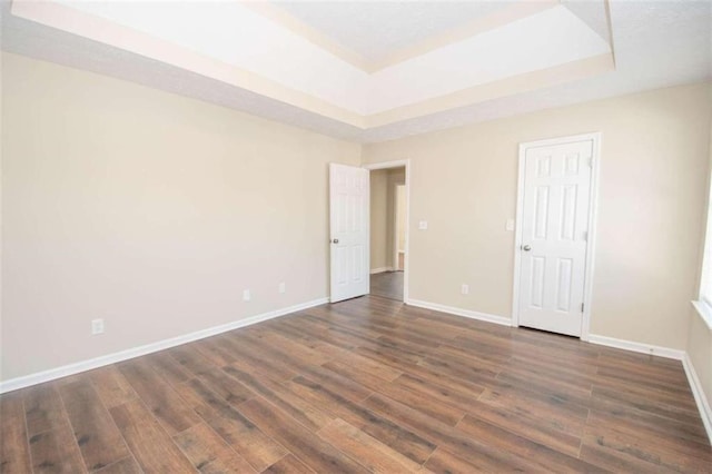 spare room featuring a tray ceiling and dark hardwood / wood-style flooring