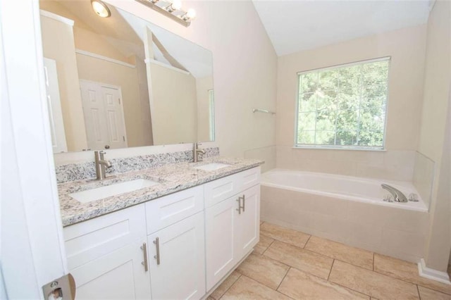 bathroom with tiled tub, vanity, vaulted ceiling, and tile patterned floors