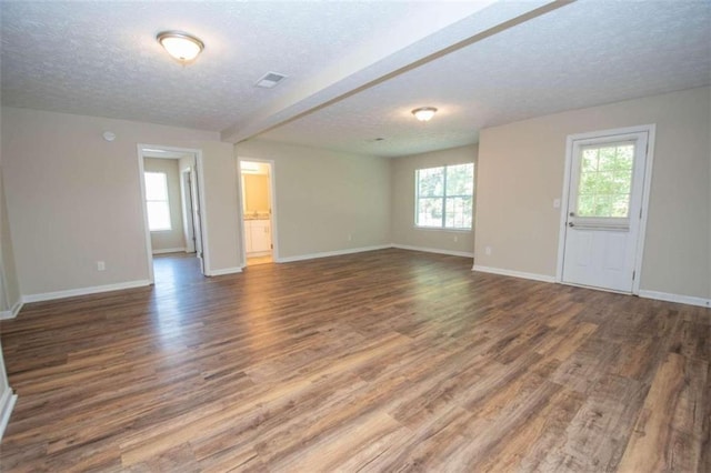 unfurnished room featuring a textured ceiling, beam ceiling, and dark wood-type flooring