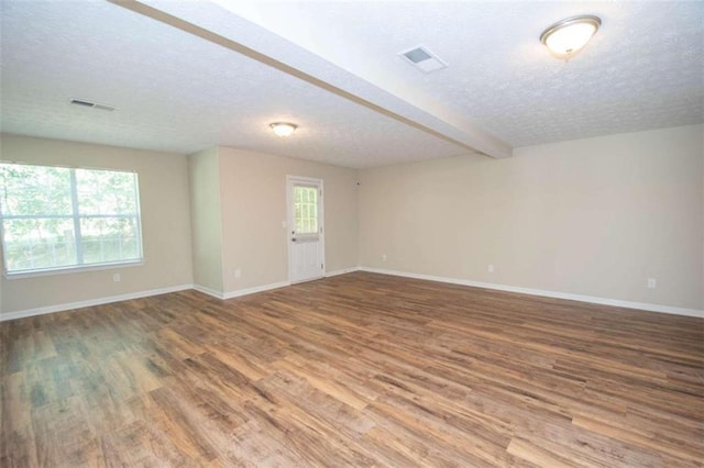 spare room featuring beamed ceiling, hardwood / wood-style flooring, a textured ceiling, and a wealth of natural light