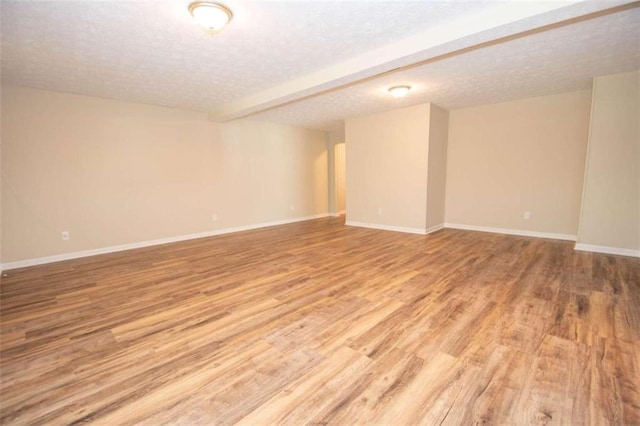 unfurnished room featuring light wood-type flooring, a textured ceiling, and beamed ceiling