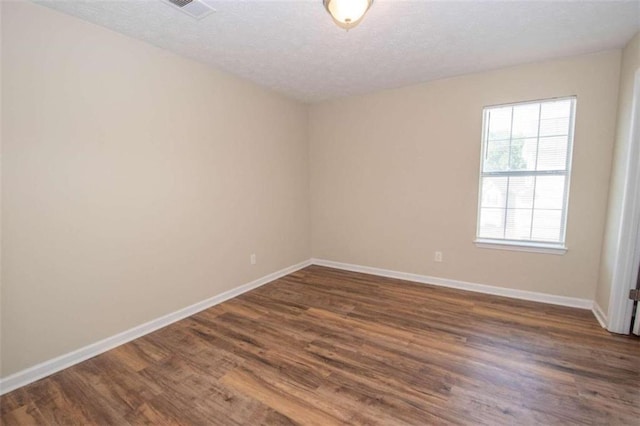 empty room with a textured ceiling and dark hardwood / wood-style flooring