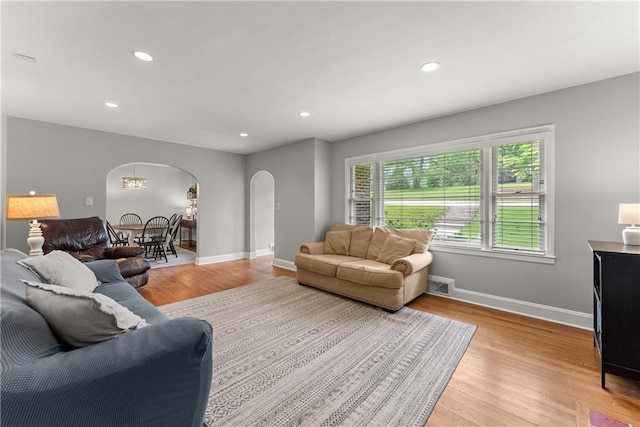 living room featuring arched walkways, light wood finished floors, baseboards, and recessed lighting