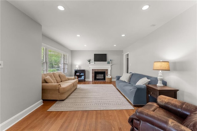 living room featuring wood finished floors, a brick fireplace, baseboards, and recessed lighting