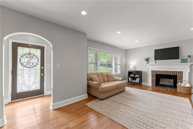 living area featuring light wood-style flooring, baseboards, a brick fireplace, and recessed lighting