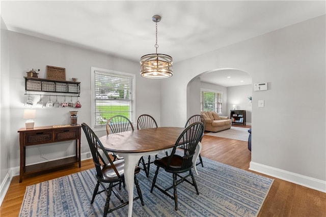 dining space featuring arched walkways, a chandelier, wood finished floors, and baseboards