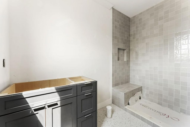 full bath featuring a tile shower, speckle patterned floor, and baseboards
