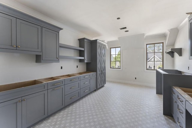 kitchen featuring open shelves, ornamental molding, gray cabinets, baseboards, and light floors