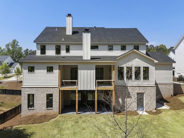 rear view of property featuring a chimney, brick siding, a lawn, and a patio