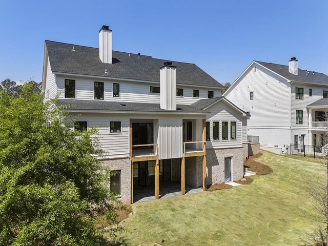 back of property featuring a chimney, a yard, roof with shingles, and brick siding