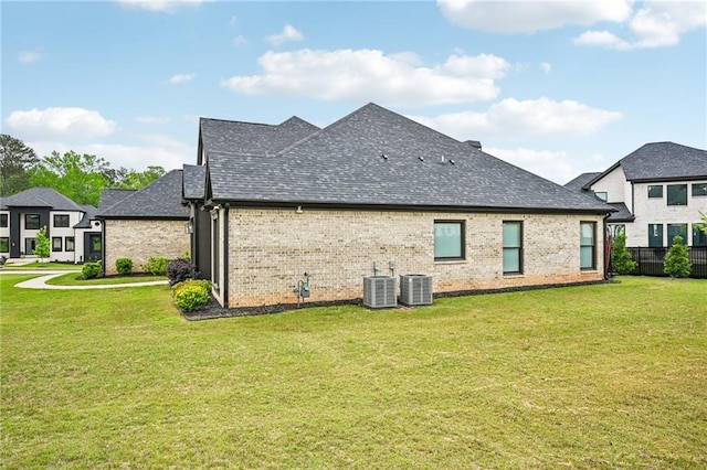 rear view of house with a shingled roof, brick siding, and central AC unit