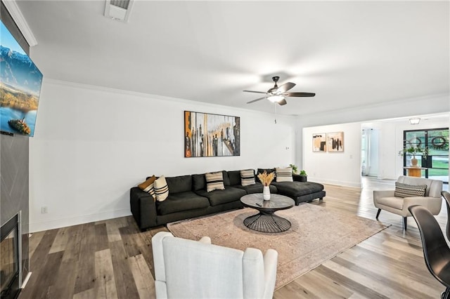 living area with a ceiling fan, wood finished floors, baseboards, and crown molding