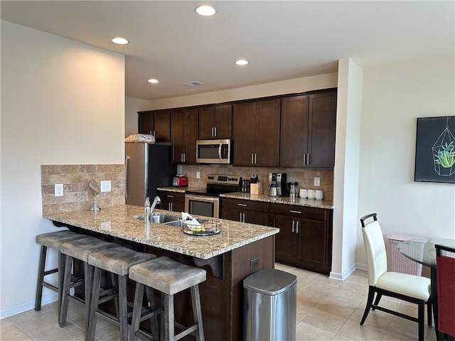 kitchen with sink, appliances with stainless steel finishes, a kitchen breakfast bar, kitchen peninsula, and decorative backsplash